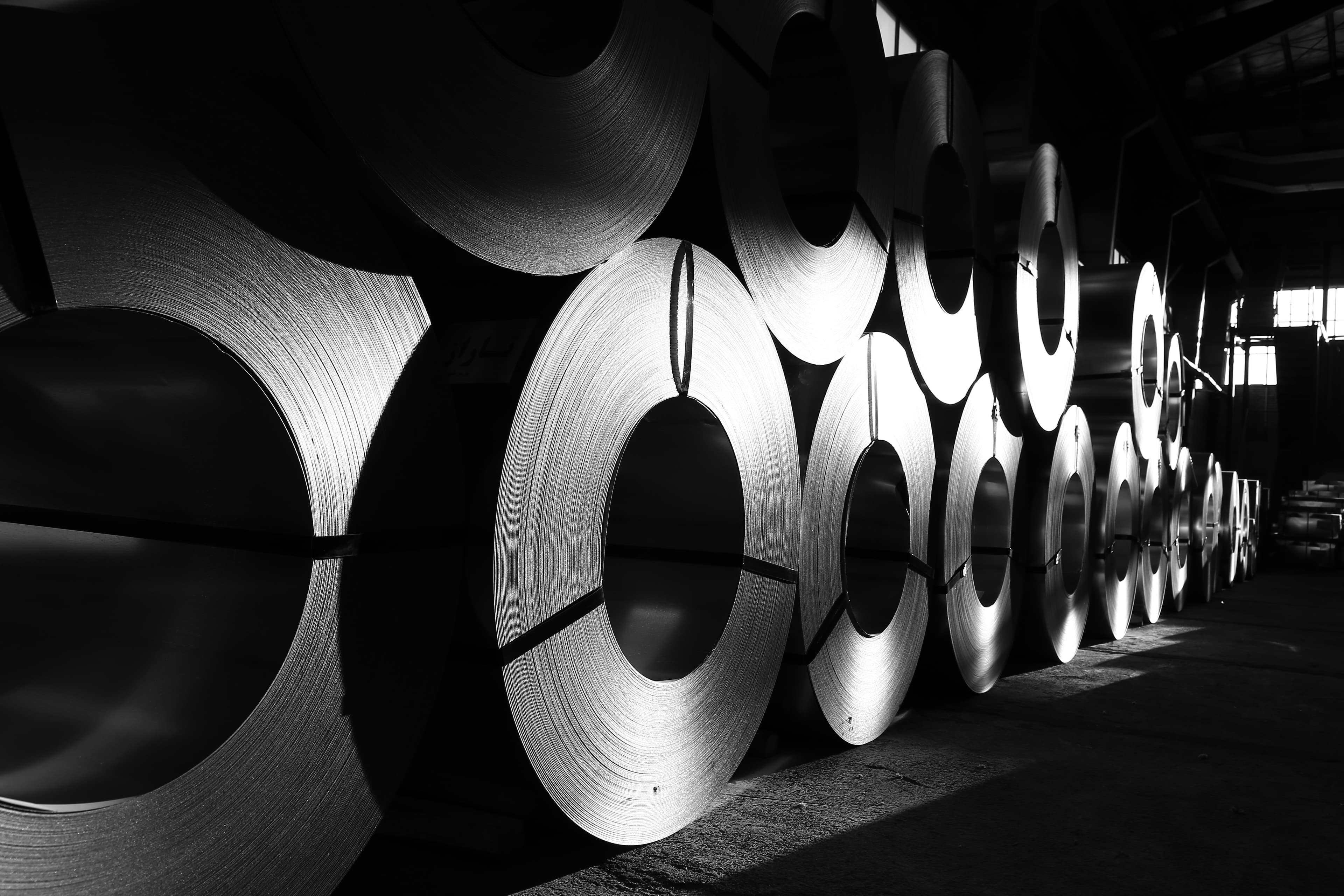 Rows of rolled steel coils staged inside an industrial warehouse