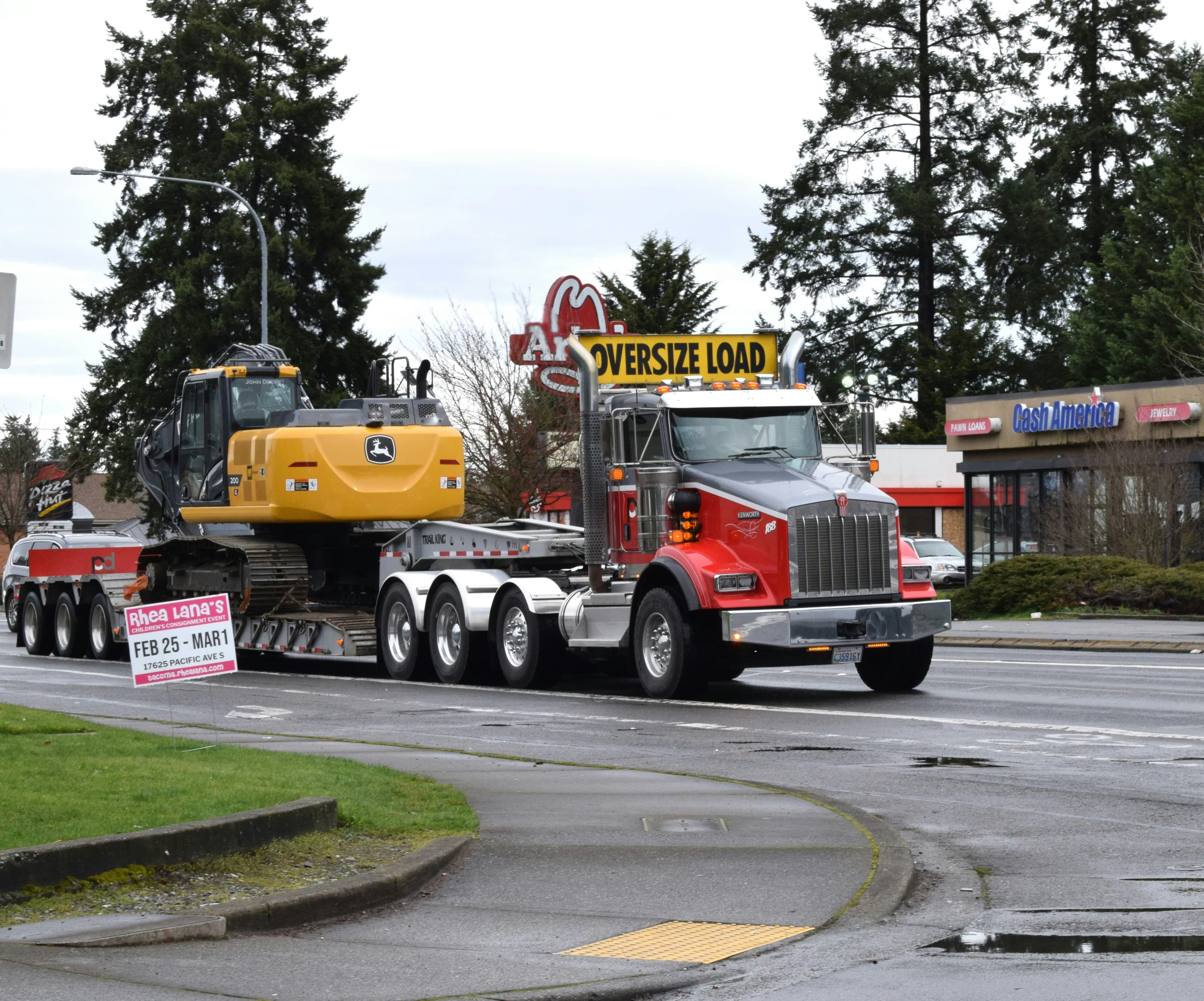 Red heavy-haul truck with an oversize load banner transporting an excavator