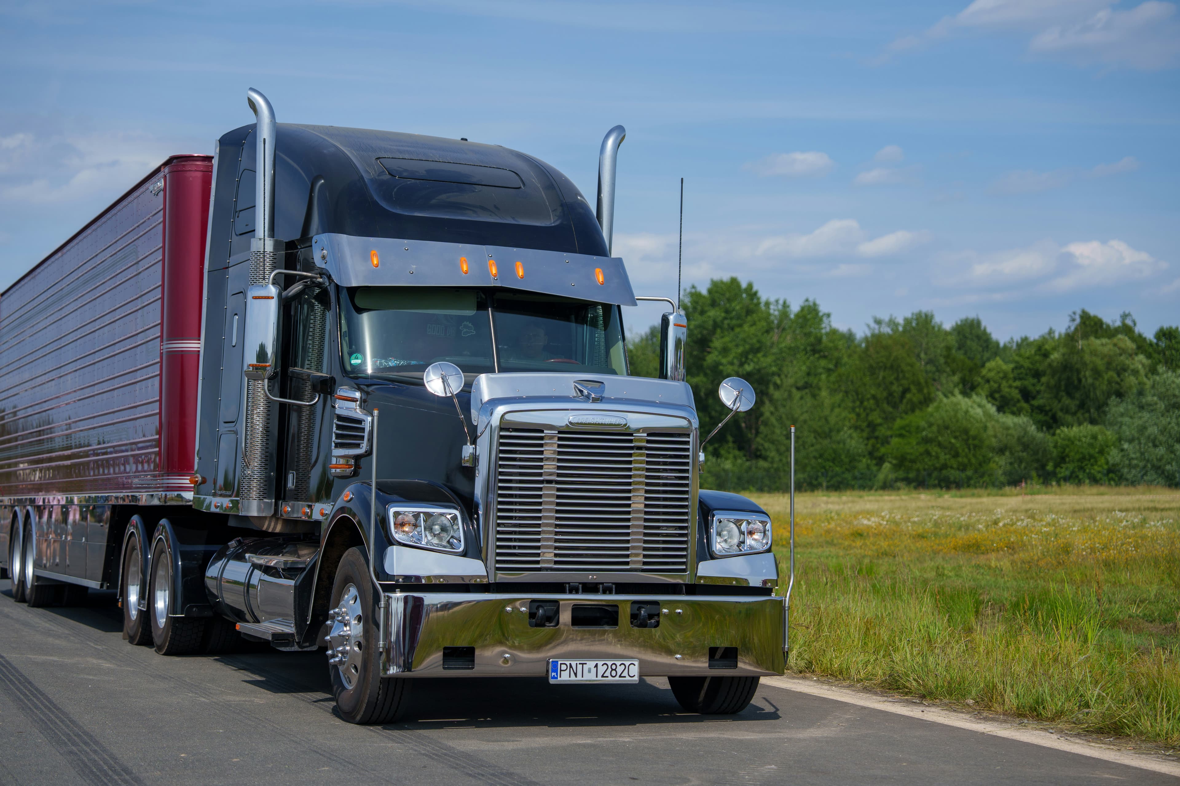 Black semi-truck pulling a 53-foot enclosed dry van trailer on a rural road