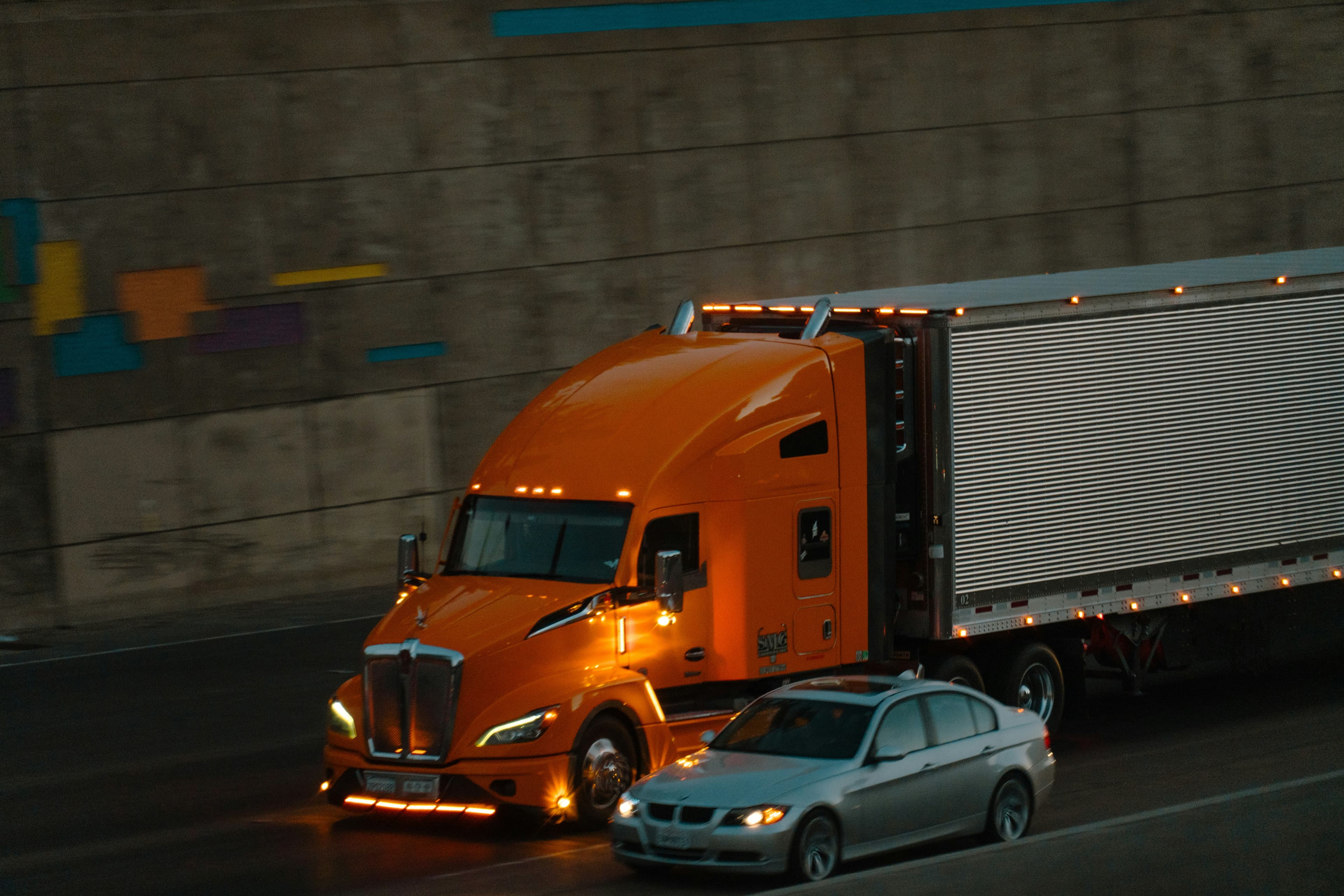 Orange semi-truck pulling an enclosed trailer on a highway at night